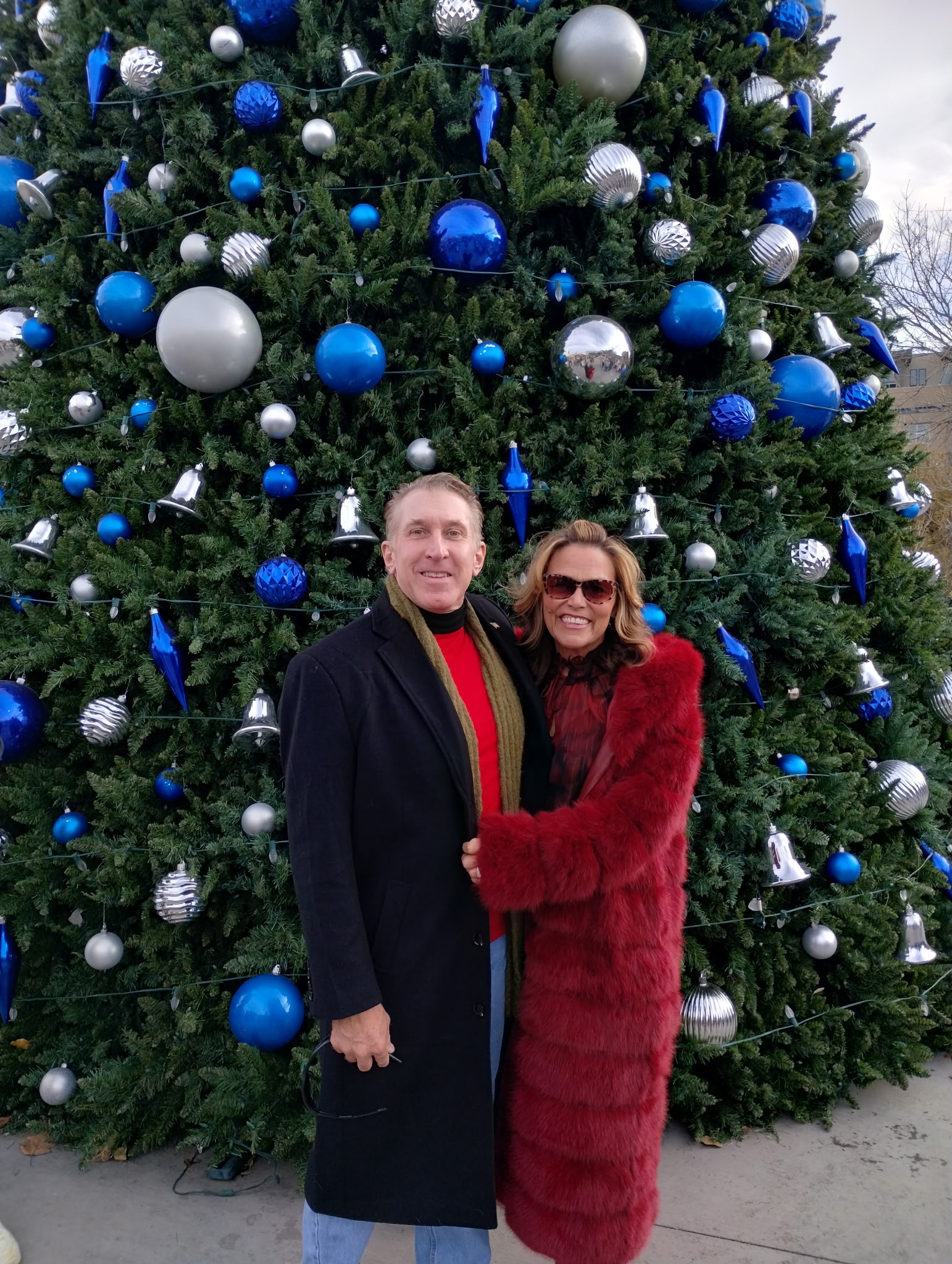 Tim Dietz and his wife JoAnna in winter coats in front of Castle Rock's towering Christmas tree decorated with blue and silver ornaments