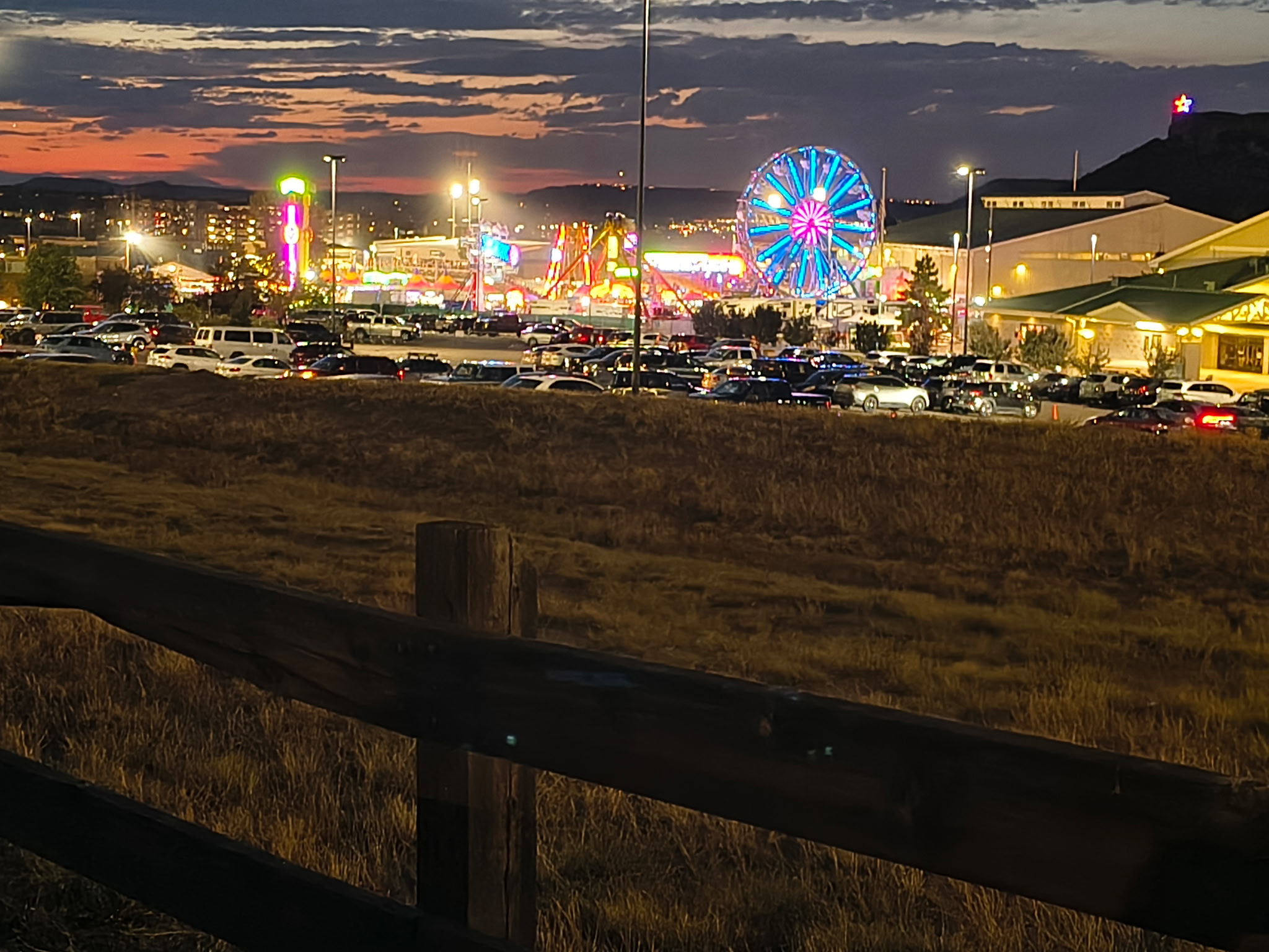 The Douglas County Fair & Rodeo carnival midway lit up at dusk in Castle Rock, with the Ferris wheel glowing and the Castle Rock star shining on the butte above