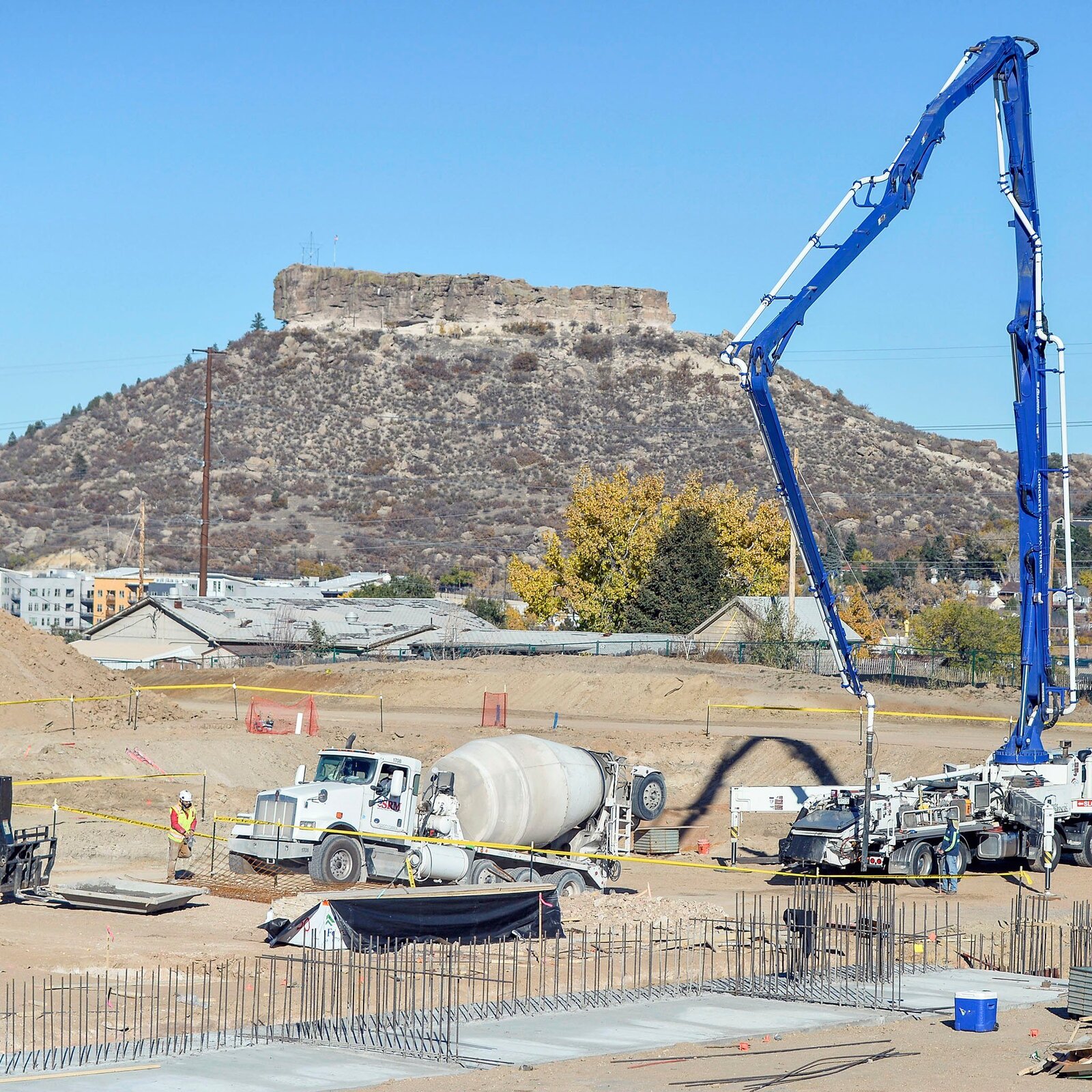 Concrete trucks and a pump boom pouring foundations at the Castle Rock Sports Center construction site, with The Rock rising in the background